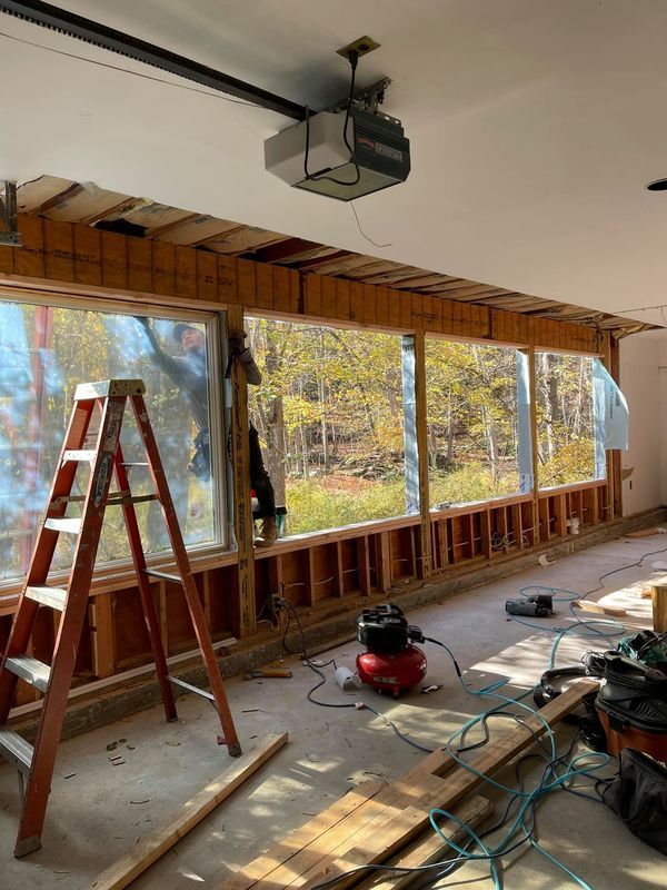 Garage renovation in progress with exposed framing and windows. Ladder, tools, and materials are visible.