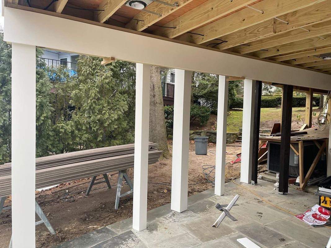 White support beams and overhead beams support a covered outdoor space. A table and yard are visible.