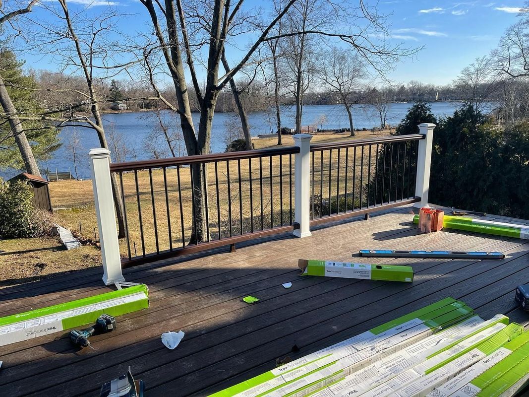 A deck overlooking a lake, with brown decking and railing, white posts, and construction materials scattered around.
