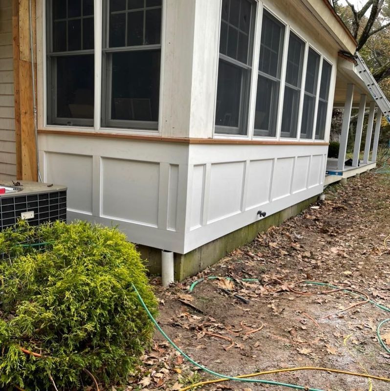 White paneled porch with screened windows and a brown trim. Air conditioning unit and foliage are in front.