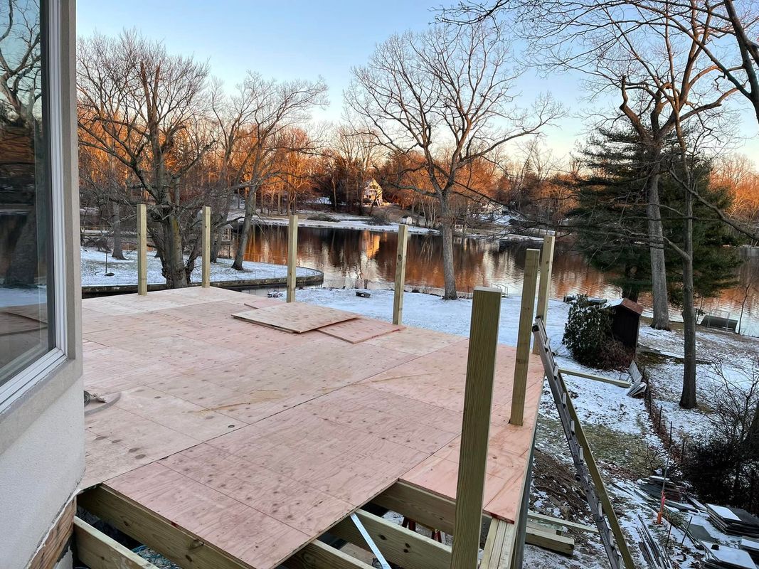 Partially constructed deck overlooking a snowy landscape and water. Wooden posts and beams are visible.