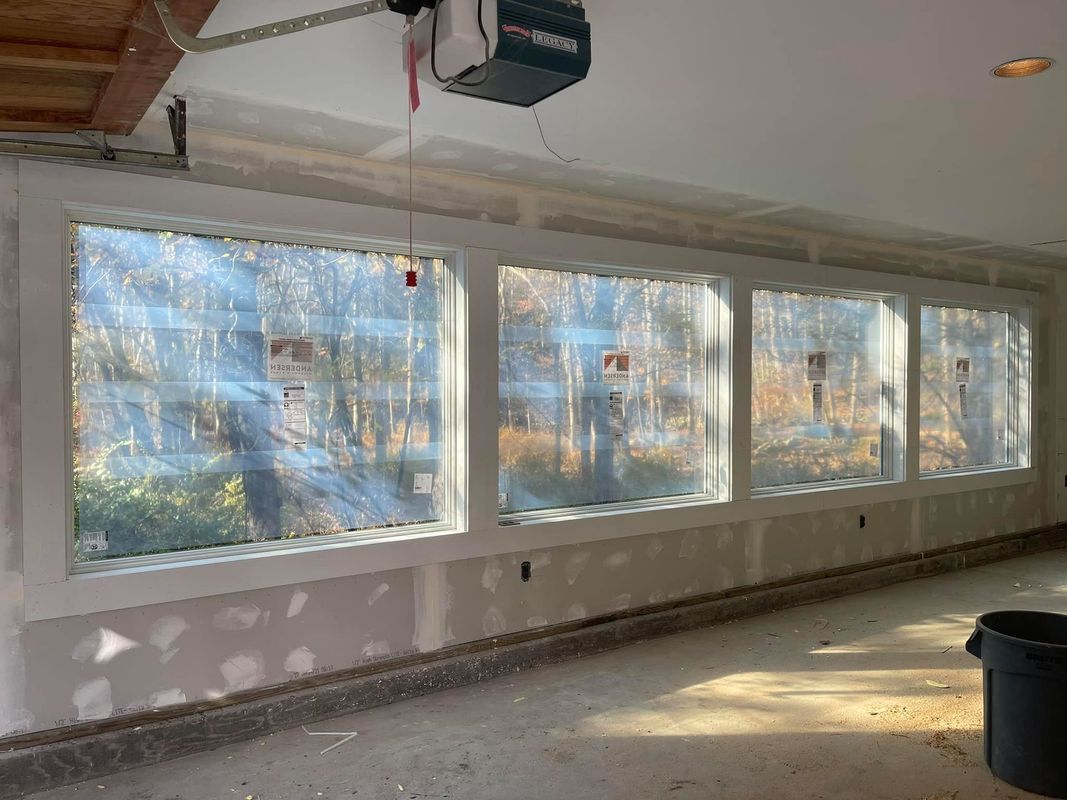 Interior view of three large windows framed in white, set in a room under construction.
