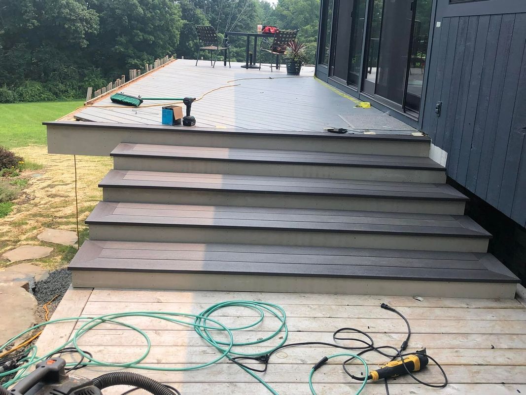 Deck and stairs under construction, featuring gray composite decking and steps. Green cables and tools visible.