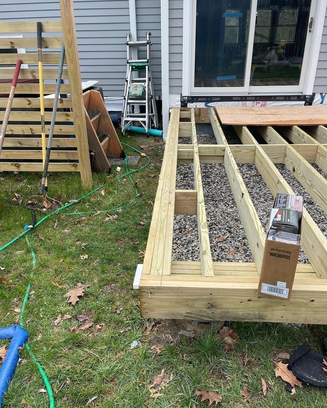 Deck under construction next to a house with tools and gravel between beams.