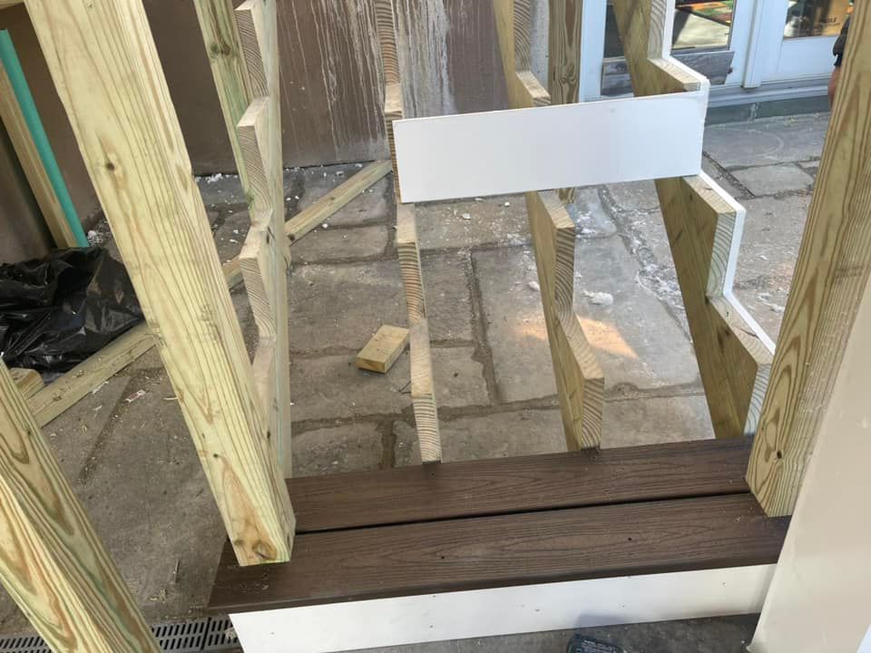 Wooden deck framework with brown boards, white and green supports, set on stone pavers.