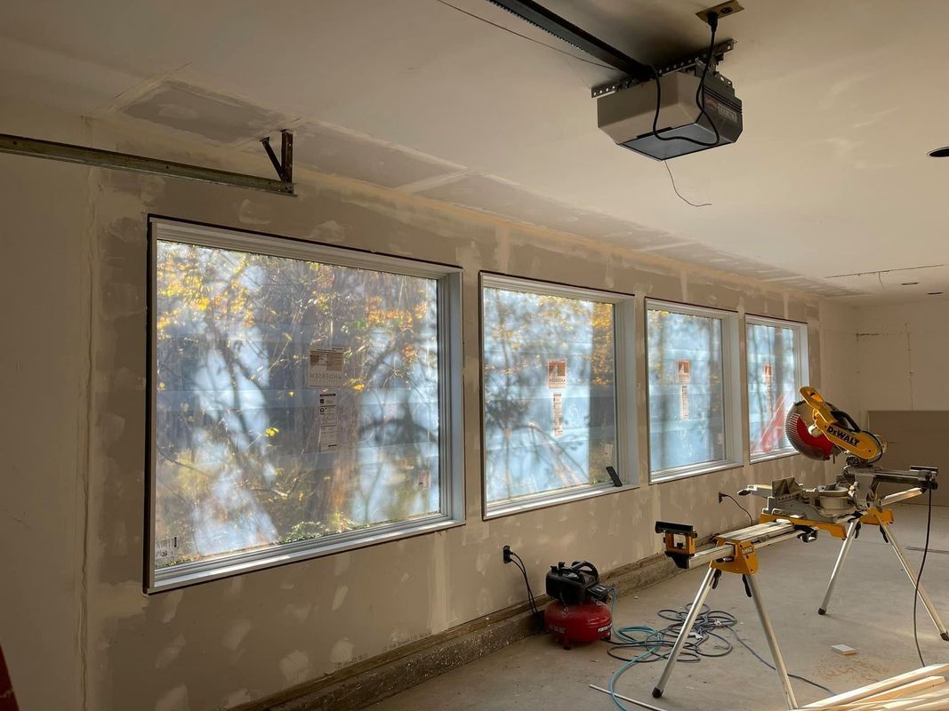 Interior of a room with three windows, a saw, compressor, and garage door opener. The windows look out onto trees.