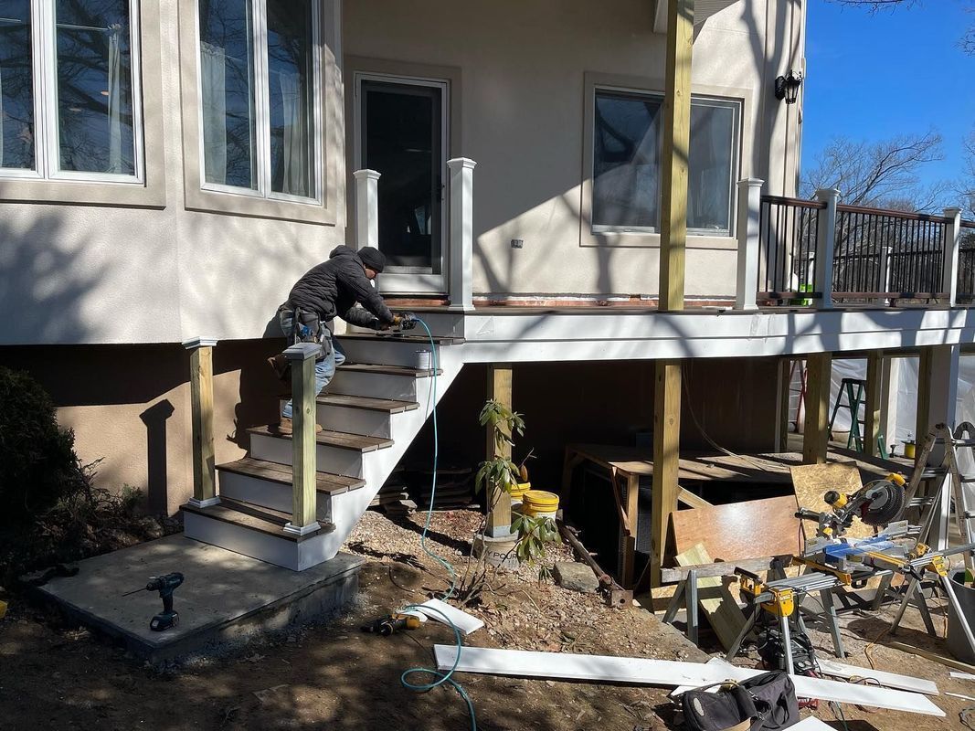 Construction worker building deck stairs on a sunny day. White house in the background.