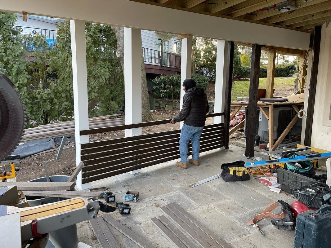 Man installing brown railing on porch, construction tools scattered.