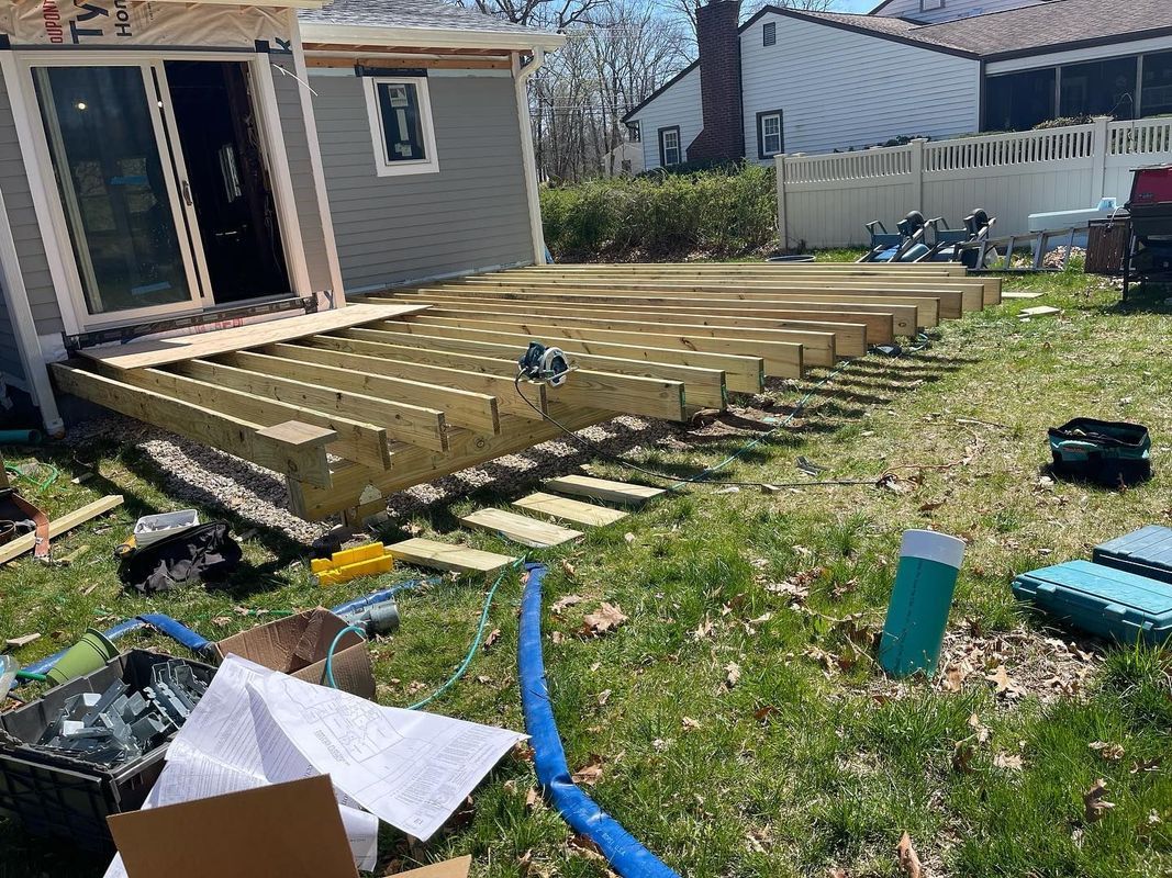 Deck construction in progress in a backyard; wooden frame with joists; tools and debris scattered.