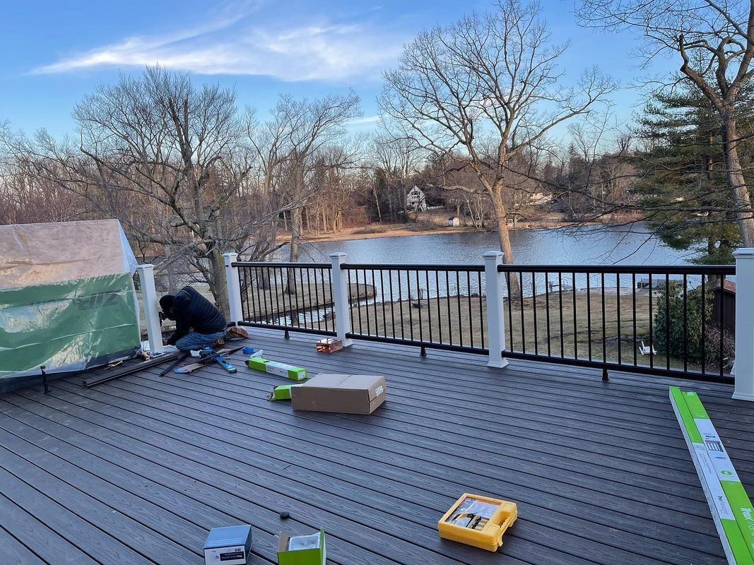 Person working on gray composite deck overlooking a lake, surrounded by trees.