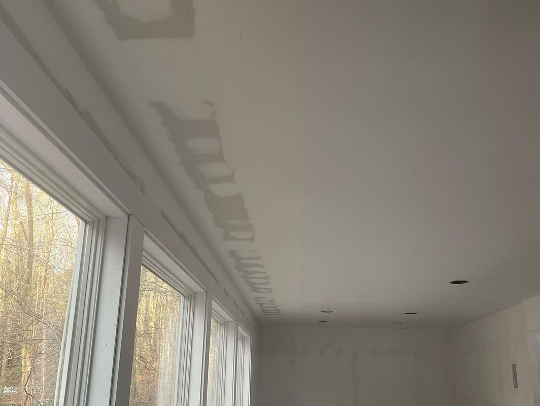 White ceiling with unfinished drywall repairs near a window and trim.