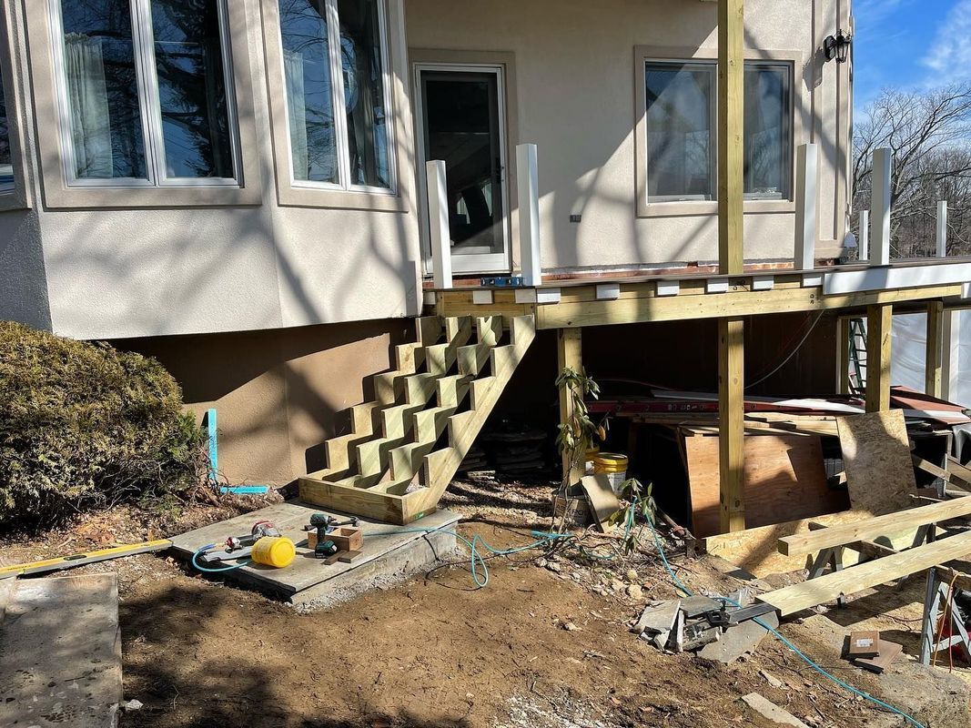 Deck stairs under construction next to a house with large windows.