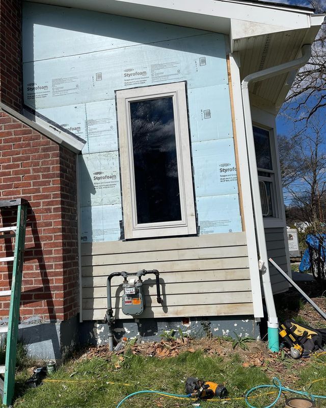 Exterior house wall under renovation with a window and gas meter. Blue insulation visible.