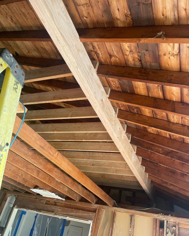 Wooden roof structure with beams and planks, viewed from below. A ladder is visible.