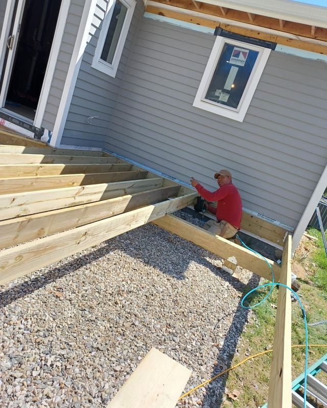 Construction worker building a wooden deck next to a house with gray siding.