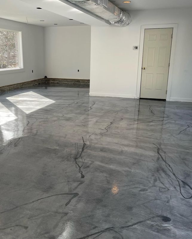 Shiny gray epoxy floor with black veining in a room with white walls and a closed door.