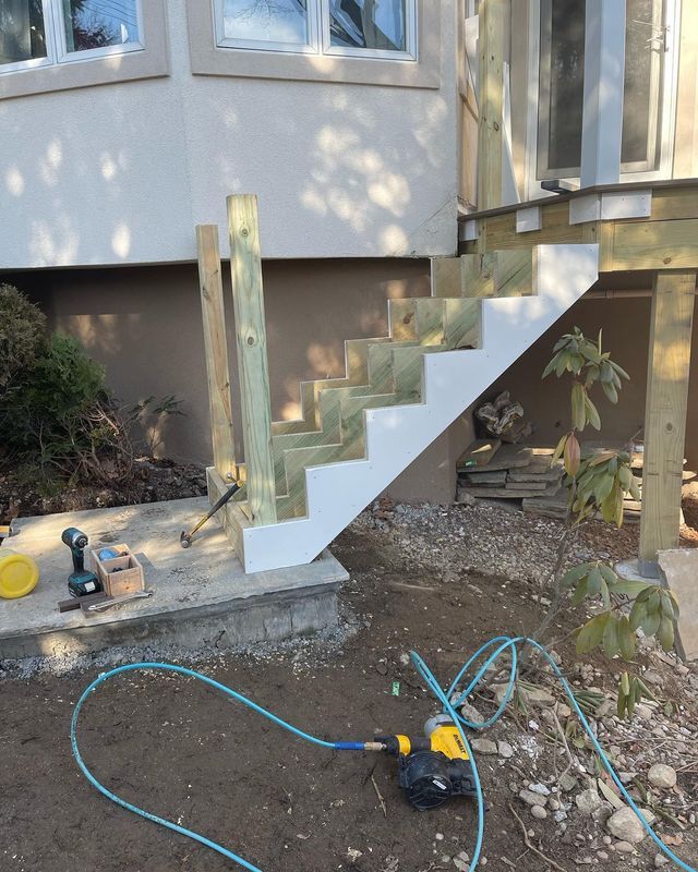 Newly constructed wooden outdoor stairs with white risers. A drill, hose, and other tools are in the dirt nearby.