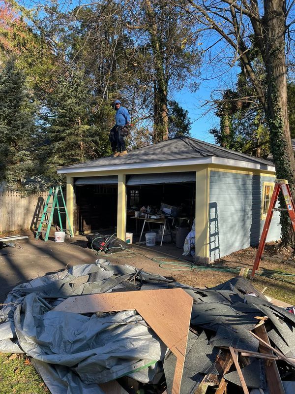 Person on a garage roof, surrounded by tools and construction debris. Garage is painted blue and yellow.