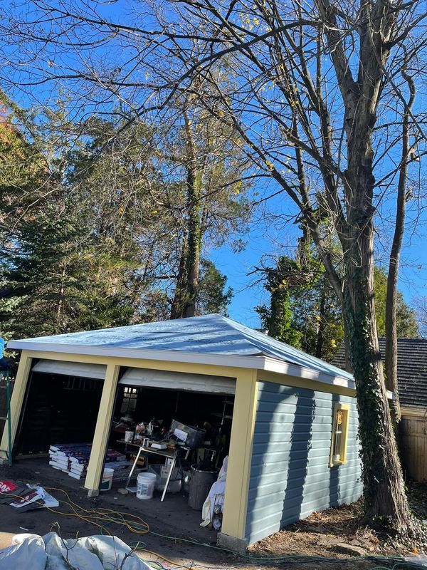 Blue and yellow garage with open doors, cluttered interior, trees, and blue sky.
