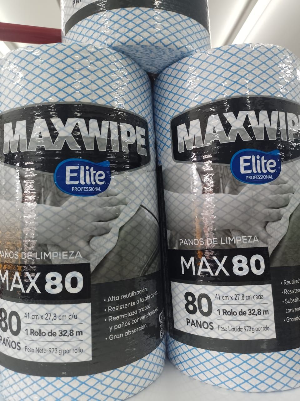Tres rollos de paños de limpieza Elite MaxWipe azules con estampado de cuadrícula en un estante.