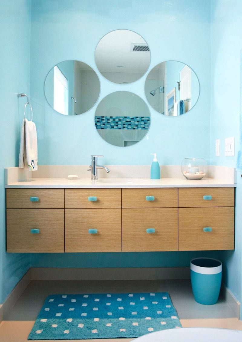 A bathroom with a sink , mirrors , drawers and a trash can.