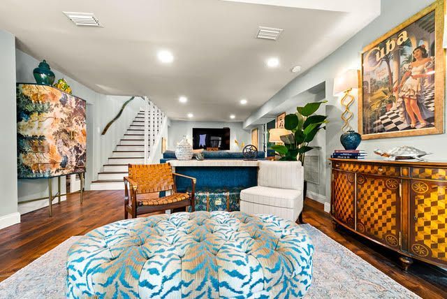 A living room with a blue ottoman , chairs , and stairs.