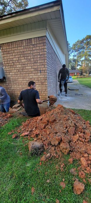 A group of men are digging a hole in the ground in front of a brick house.