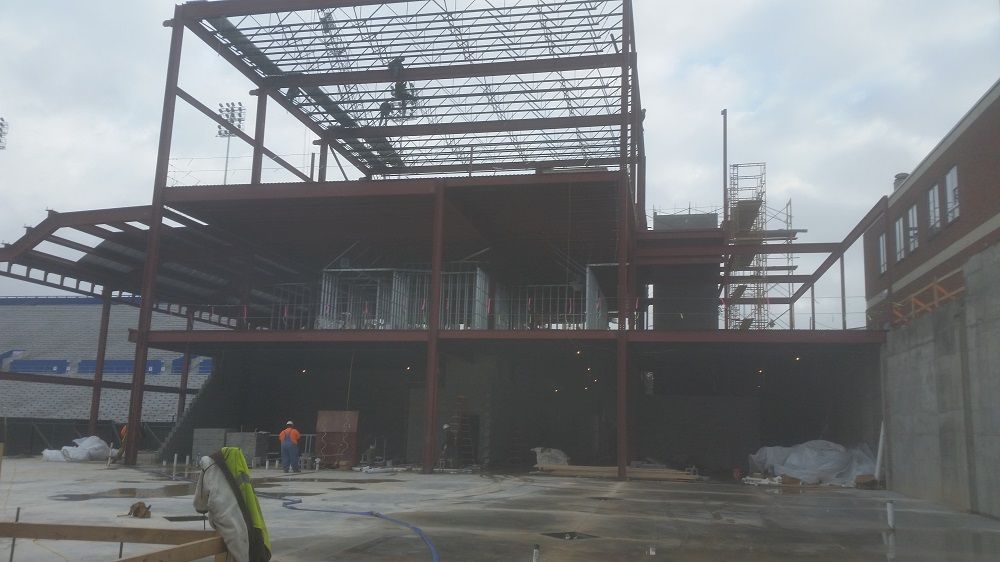 A large building under construction with a brick building in the background