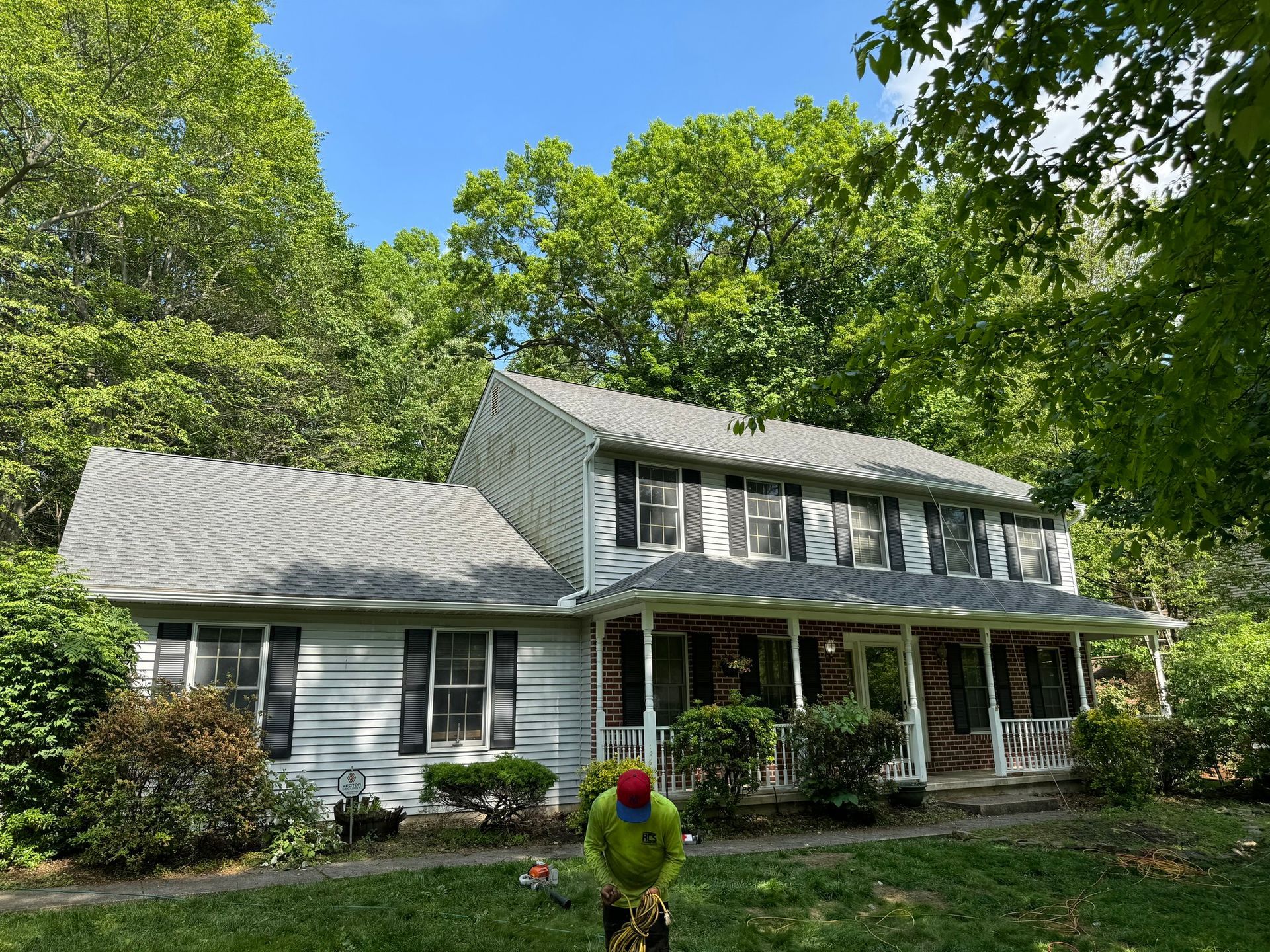 A man is standing in front of a white house with a porch.