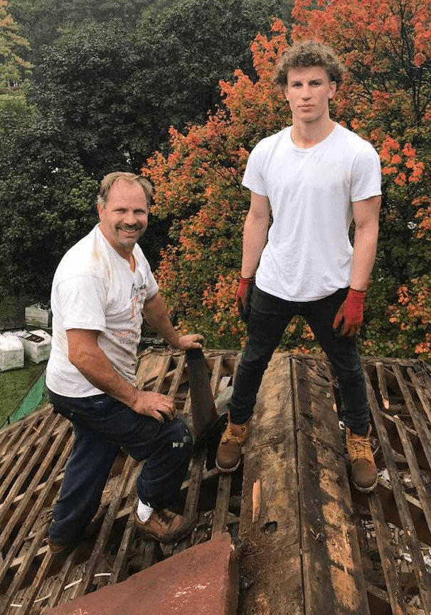 Two men are standing on top of a wooden roof.