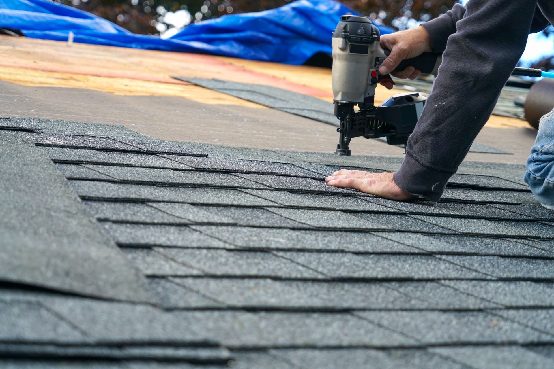 Person nailing shingles on a roof.