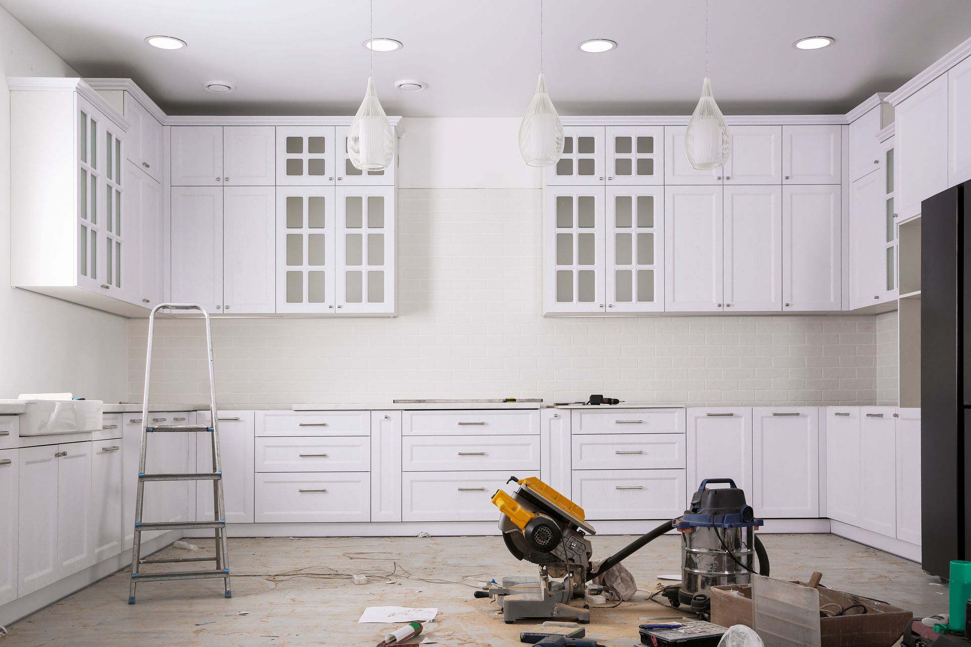 A kitchen under construction with white cabinets and a ladder.