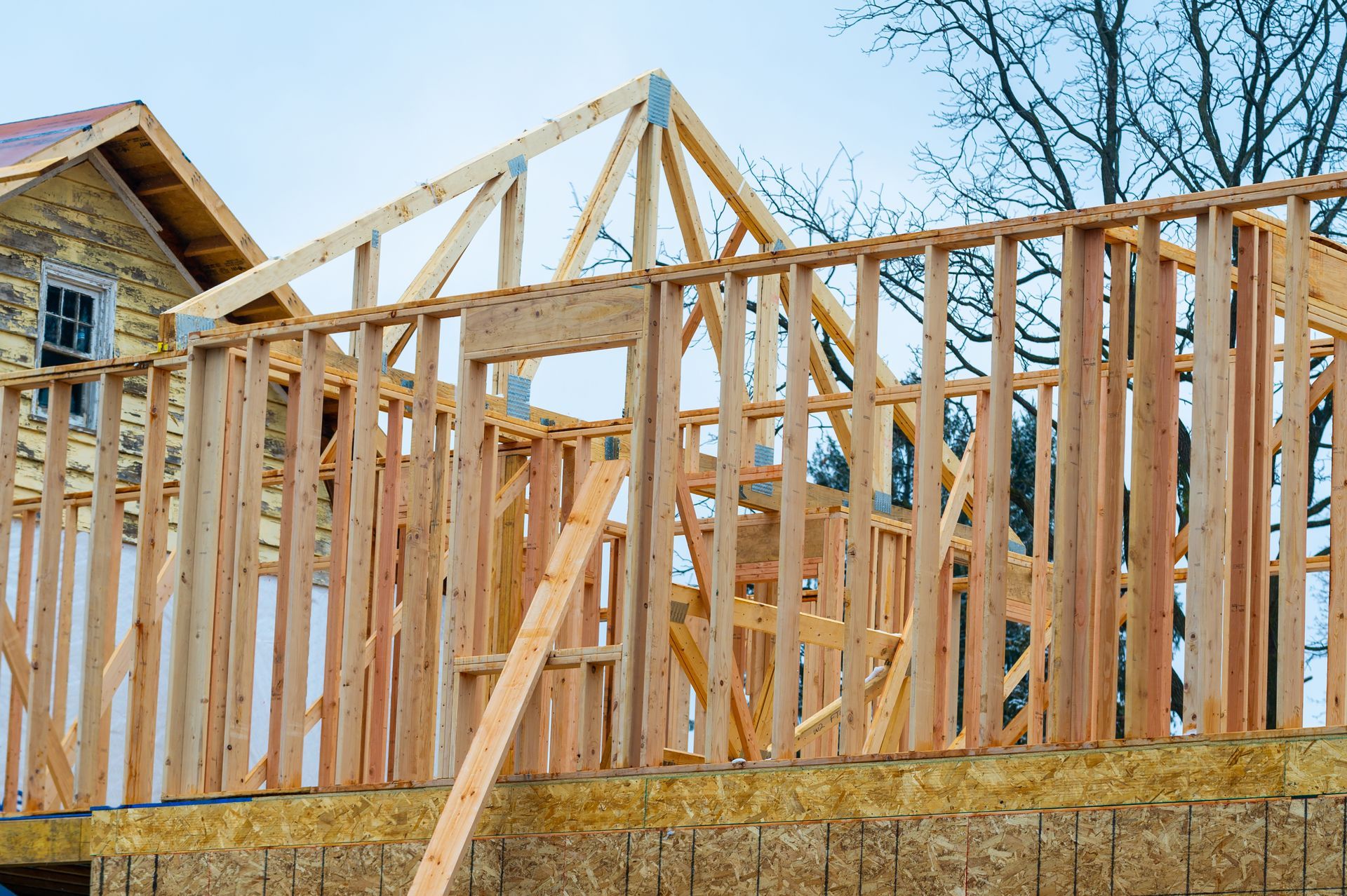 Wood-framed house under construction with exposed trusses and stone foundation