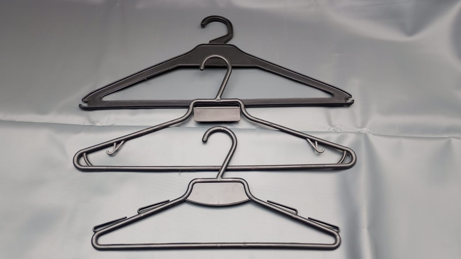 Tres perchas de plástico de color negro y gris dispuestas verticalmente sobre una superficie de color azul claro.