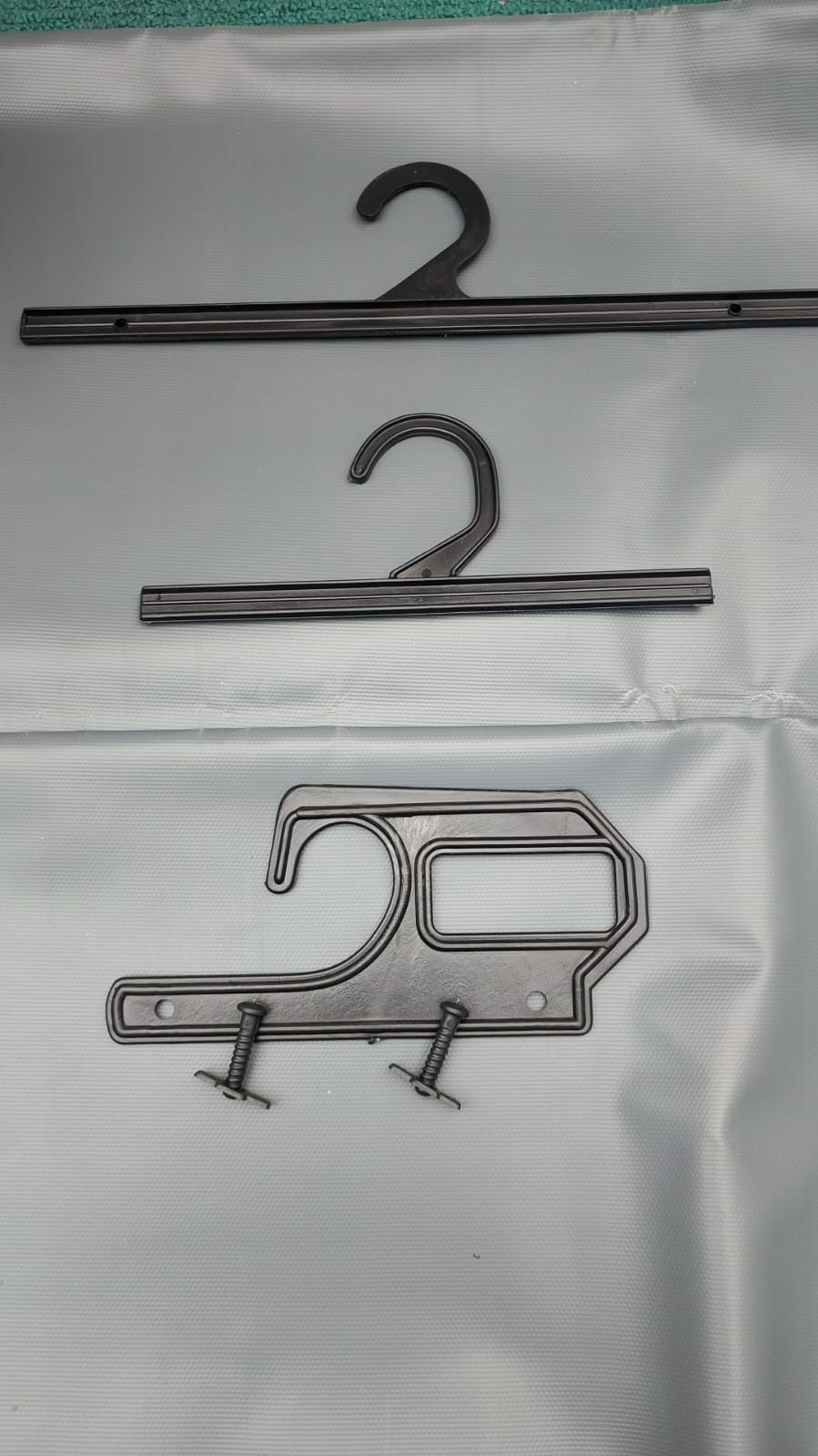 Tres perchas de ropa de plástico negro sobre un fondo de tela azul claro.