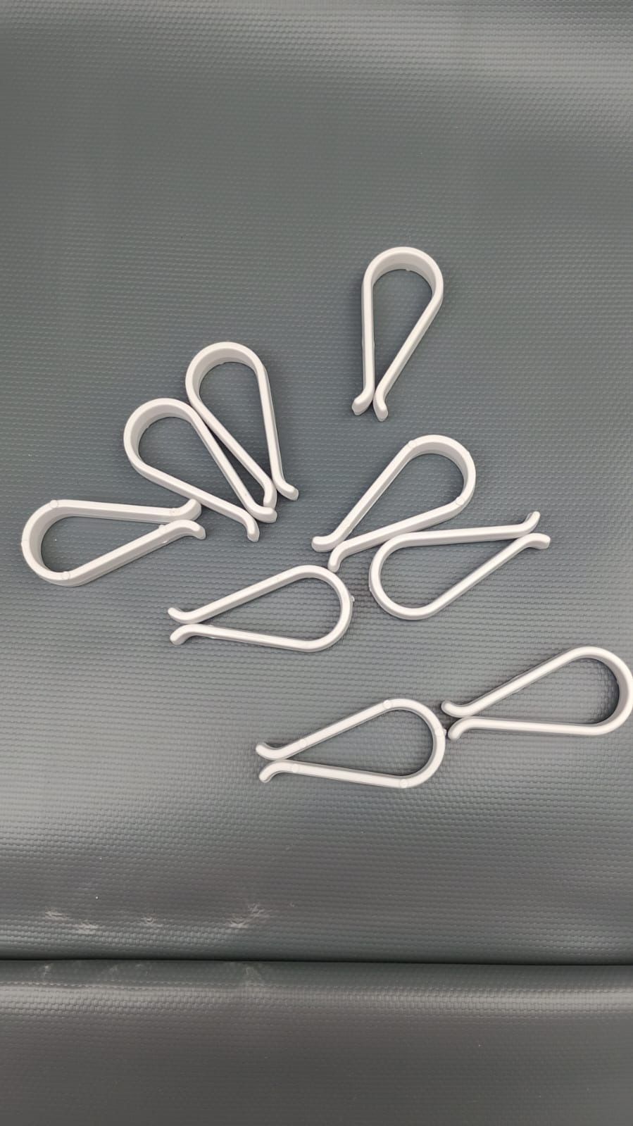 Diez pinzas de corbata de plástico blanco sobre una superficie gris.