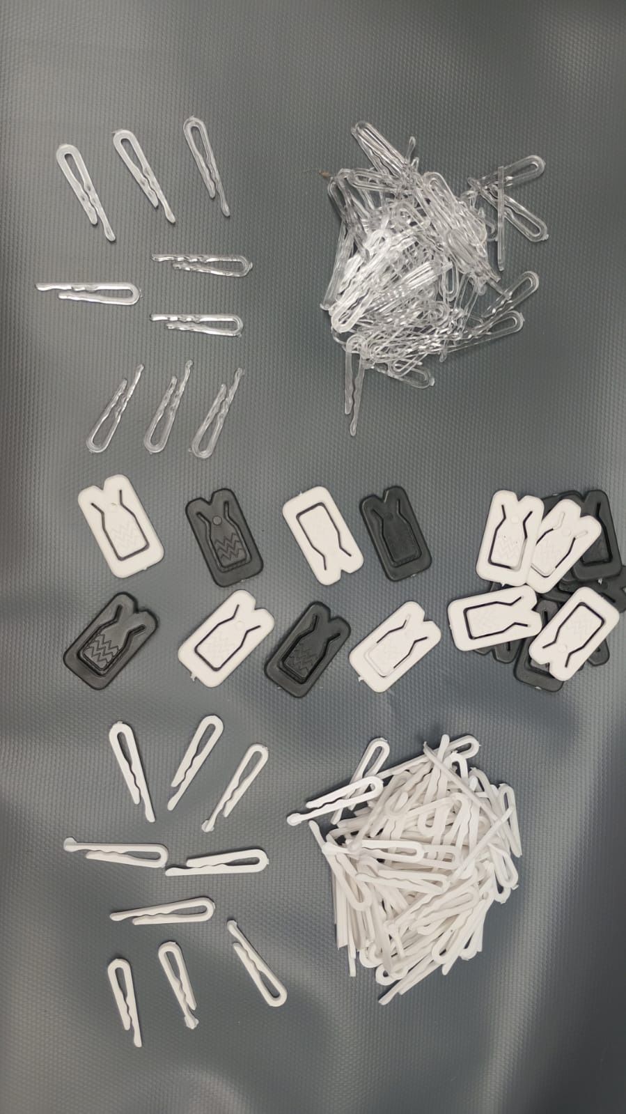 Disposición de diversos accesorios para el cabello: horquillas de metal y pinzas de plástico en color blanco, transparente y negro sobre una superficie gris.