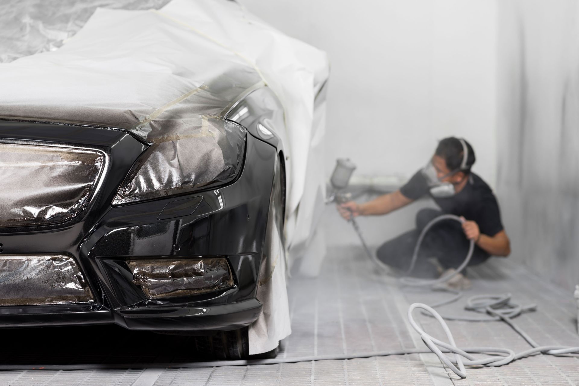 A man is spray painting a black car in a garage.