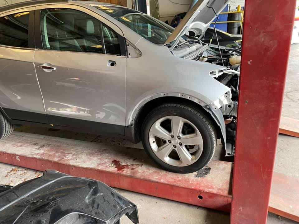 A silver car is sitting on a lift with its hood open.