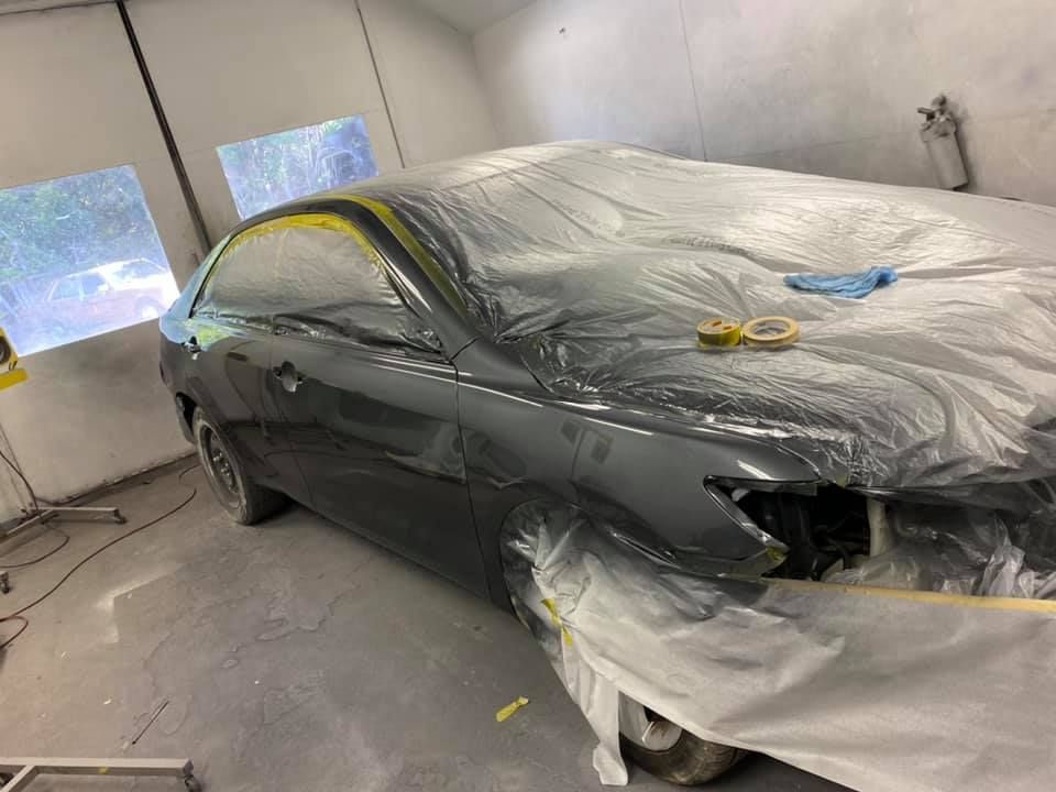 A car is covered in plastic in a paint booth.