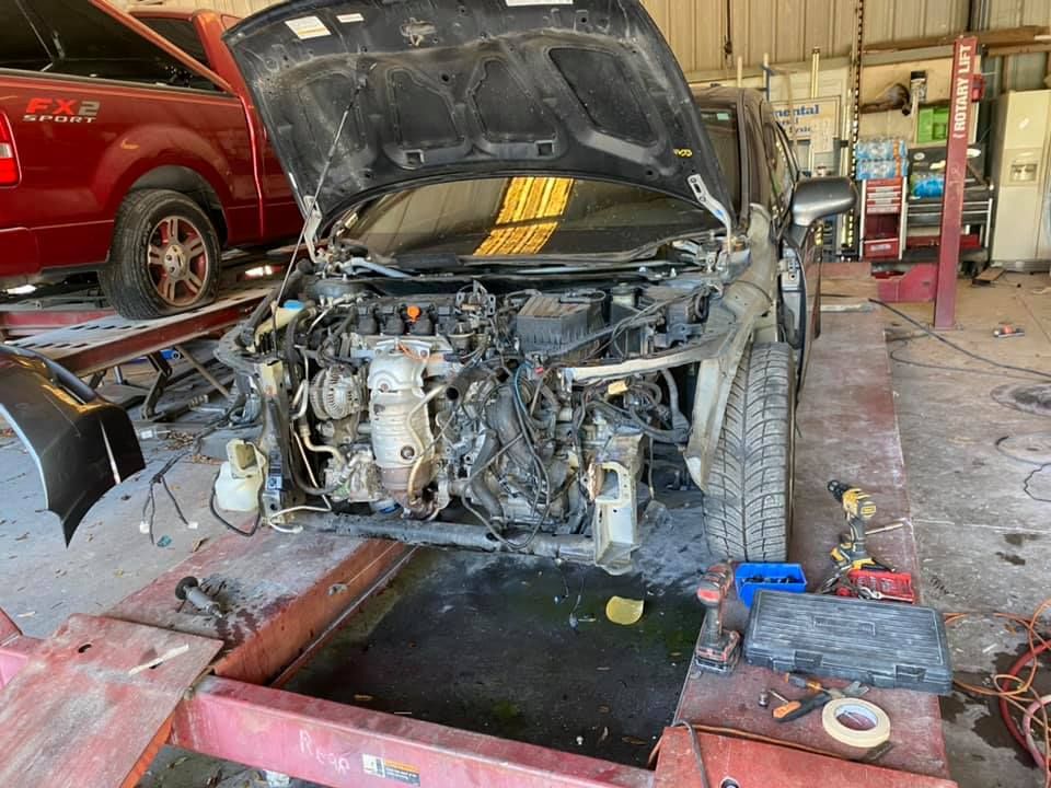 A car with the hood up is being worked on in a garage.