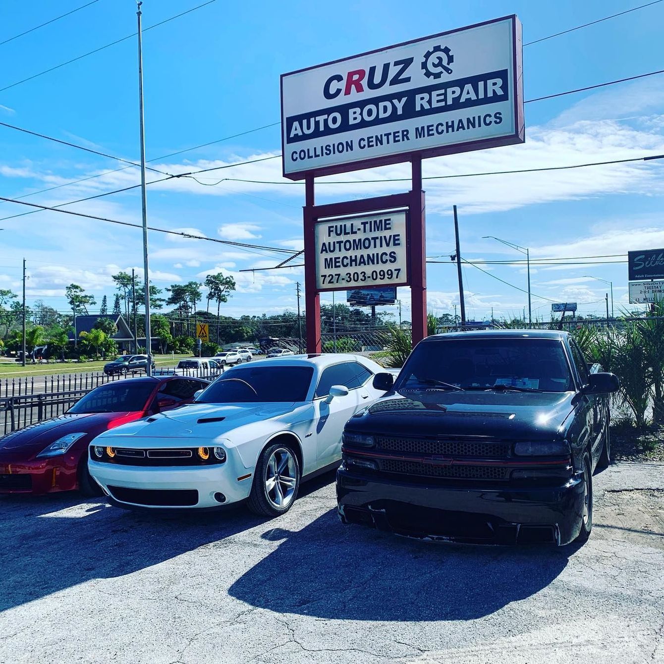 A group of cars are parked in front of a sign for cruz auto body repair.