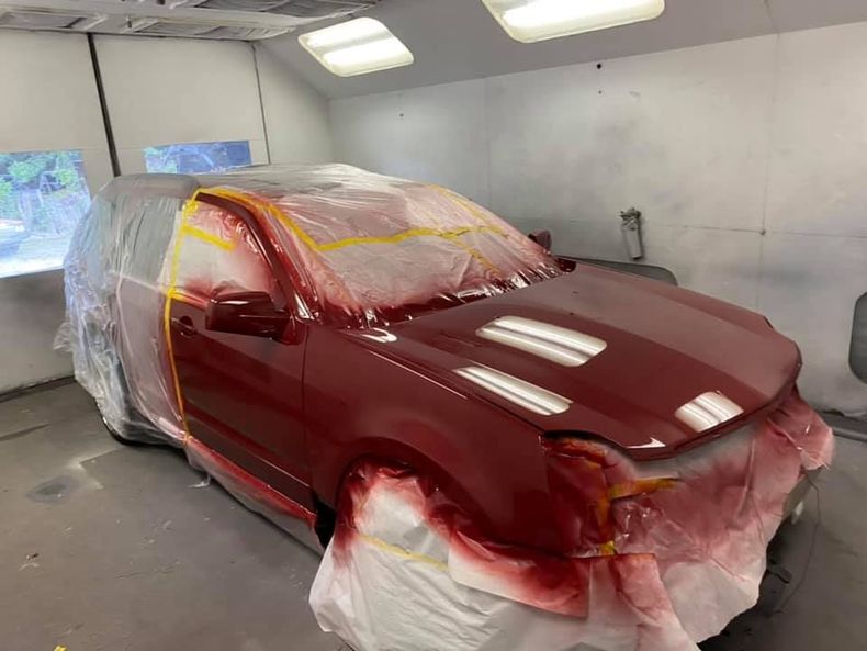 A red car is being painted in a paint booth.