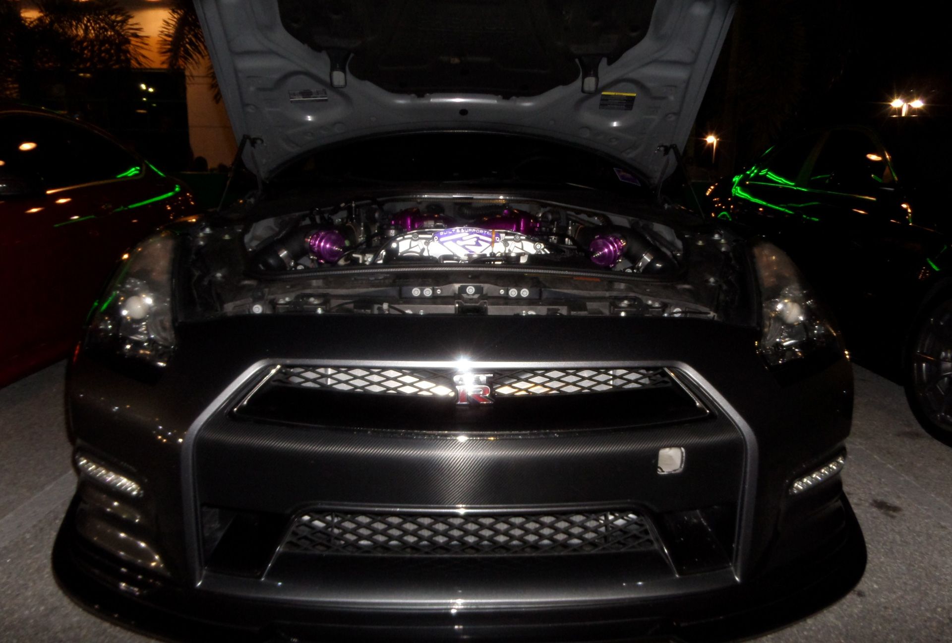 A black car with the hood up is parked in a garage.