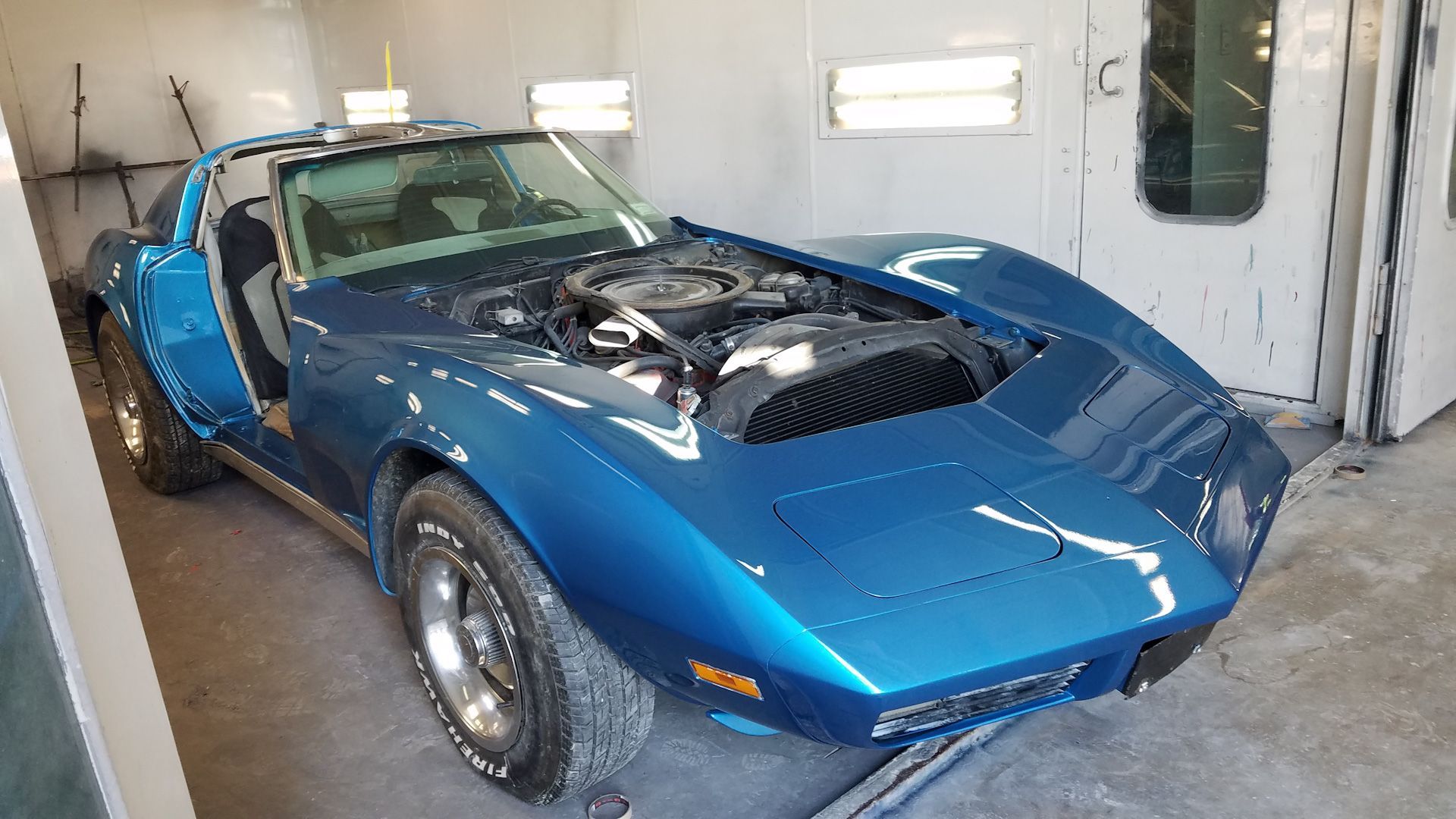 A blue corvette is parked in a garage with the hood open.