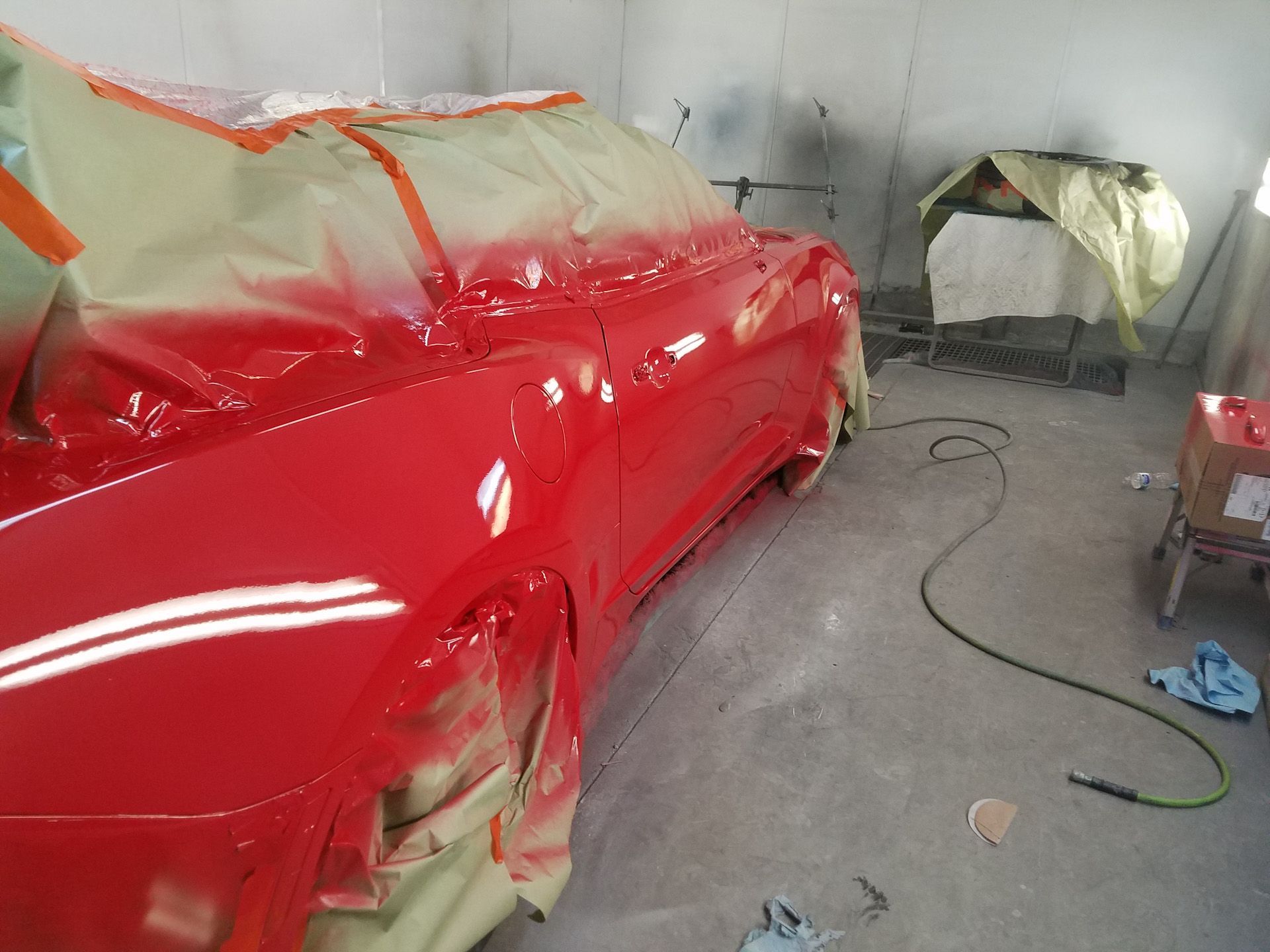 A red car is being painted in a paint booth