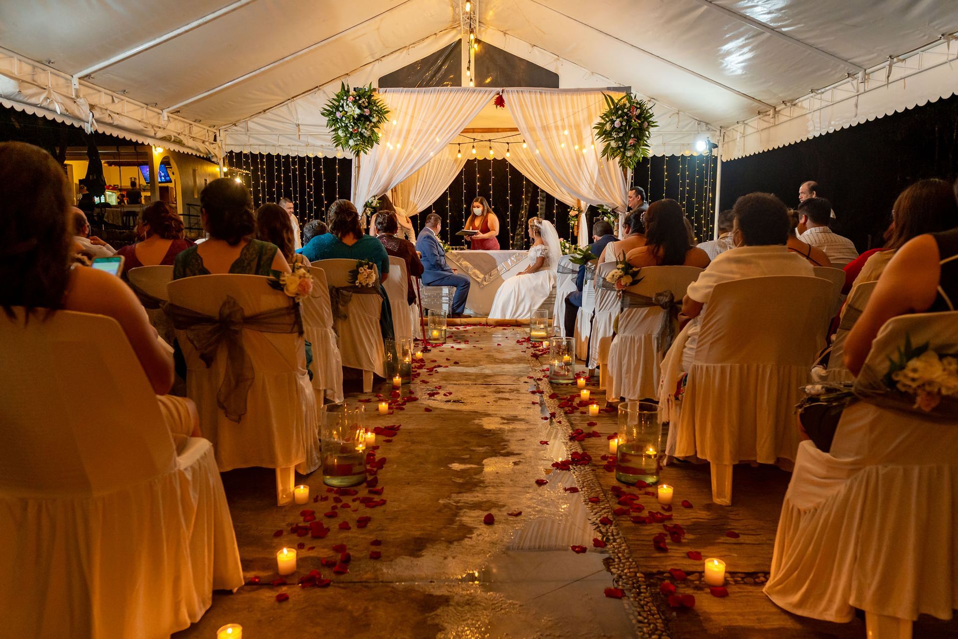 Un grupo de personas están sentadas en sillas bajo una carpa en una ceremonia de boda.