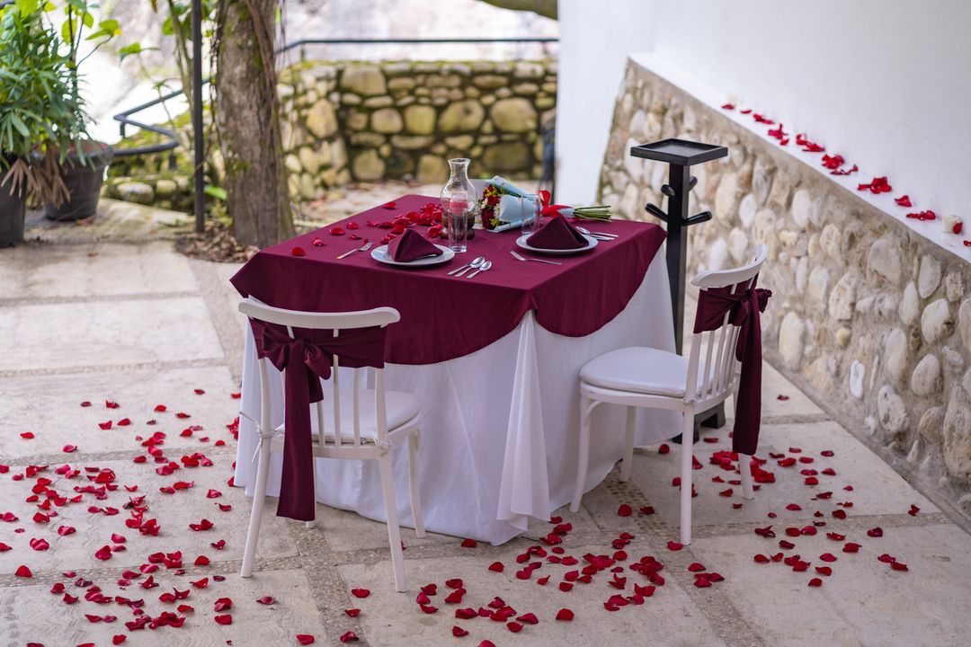 Una mesa con un mantel color burdeos y pétalos en el suelo.