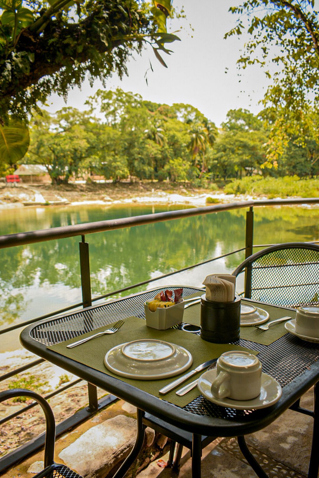 Una mesa con platos, tazas, utensilios y una vista de un lago.
