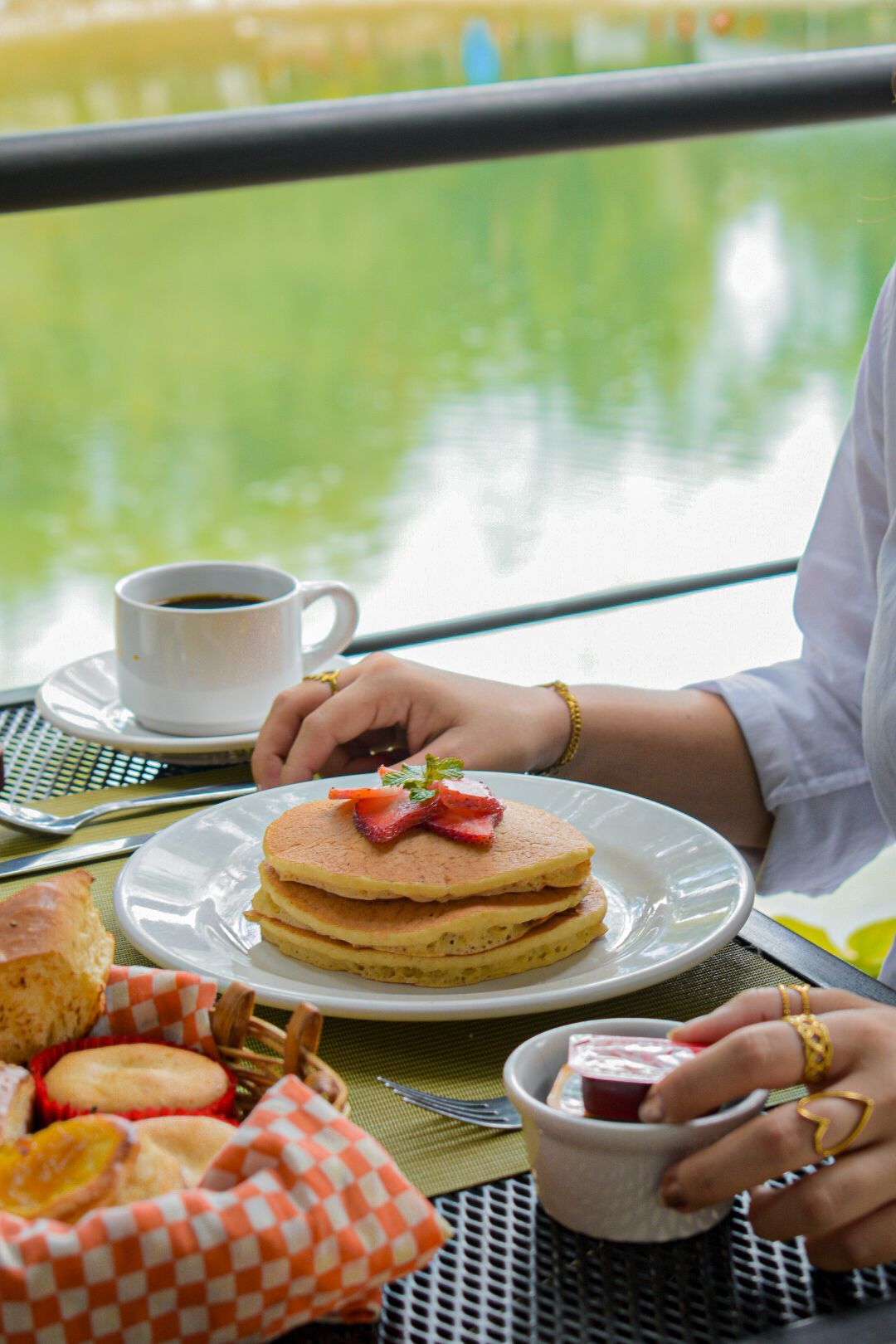 Una mujer está sentada en una mesa con un plato de panqueques y una taza de café.